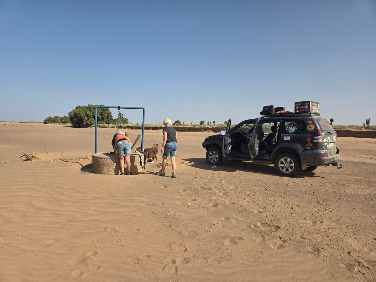 Travelers and a guide beside a 4x4 vehicle at a desert well in Merzouga Morocco during a Sahara driving experience with Merzouga Morocco activities