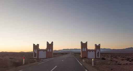 2-Day Tour from Boumalne Dades entrance gate with traditional Moroccan architectural towers at sunrise over desert landscape and road