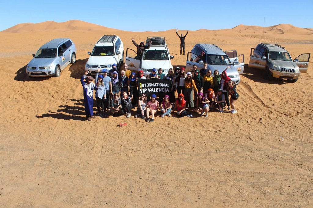 Group of tourists posing in front of five SUVs on orange sand dunes under a clear blue sky on a 2-Day Tour from Boumalne Dades