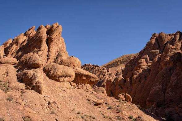 Rocky desert landscape with reddish sandstone formations under a clear blue sky during a 2-Day Tour from Boumalne Dades
