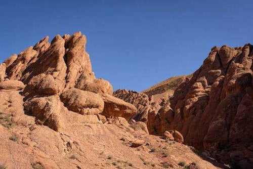 Rocky desert landscape with reddish sandstone formations under a clear blue sky during a 2-Day Tour from Boumalne Dades