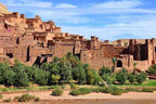 Ancient brown earthen kasbah with traditional Moroccan architecture surrounded by green palm trees under a blue sky in southeastern Morocco on 2-Day Tour from Marrakech