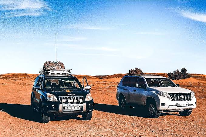 Two off-road SUVs, one black and one white, parked on sandy desert terrain with clear blue sky during 2-Day Tour from Marrakech