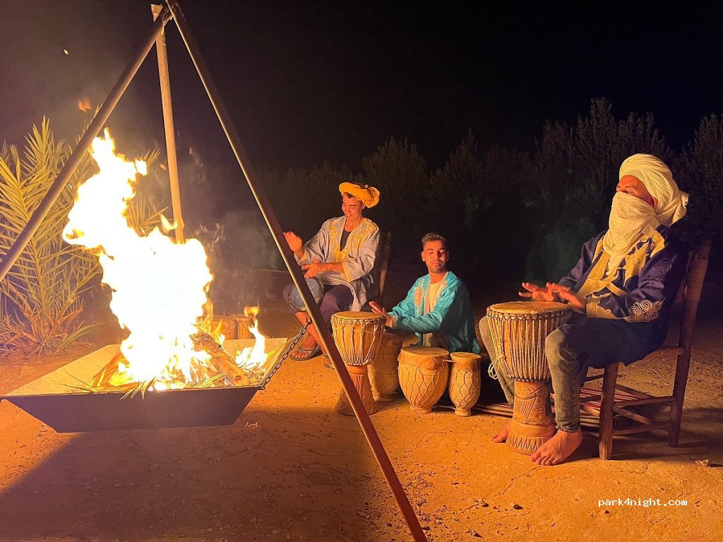 Traditional Moroccan men playing drums by a campfire at night on sandy ground during a 2-Day Tour from Marrakech