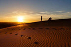 Sahara Desert golden sand dunes at sunset with two silhouetted children and visible footprints in sand