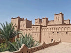 Traditional mud-brick kasbah with intricate geometric patterns and palm trees under a clear blue sky, illustrating a 2-Day Tour from Marrakech
