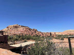 View of the historic Ait Ben Haddou fortress with brown clay buildings on a hill under a clear blue sky, showcasing the 2 day tour from Merzouga to Marrakech.