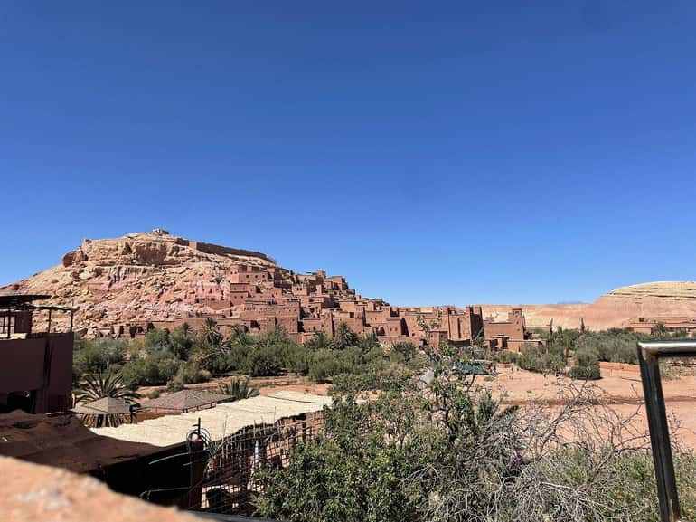 View of the historic Ait Ben Haddou fortress with brown clay buildings on a hill under a clear blue sky, showcasing the 2 day tour from Merzouga to Marrakech.