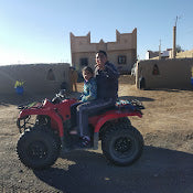 2-Hour Merzouga Quad Bike red and black quad with rider wearing blue jacket in desert village with mud brick buildings