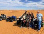 2-Hour Merzouga Quad Bike tour group with helmets standing in the orange sand dunes next to three all-terrain quad bikes under a blue sky