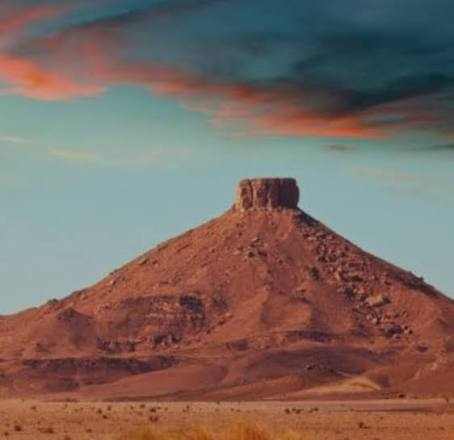3-Day Tour from Ouarzazate to Merzouga and Zagora featuring a distinctive flat-topped rocky mountain in the Moroccan desert under a colorful sky