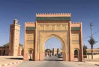 large traditional Moroccan gate with intricate geometric carvings in sandy beige stone and green tiled rooftops under clear blue sky