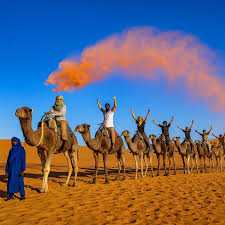 Camel caravan riding on golden sand dunes in a desert with people holding a colorful smoke flare during a 3 Days Tour