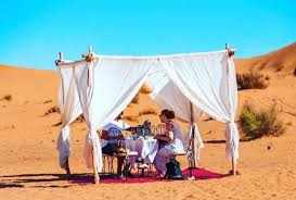 Outdoor dining setup with white fabric canopy, carpet, and table with chairs on sandy dunes during 3 Days Tour in desert
