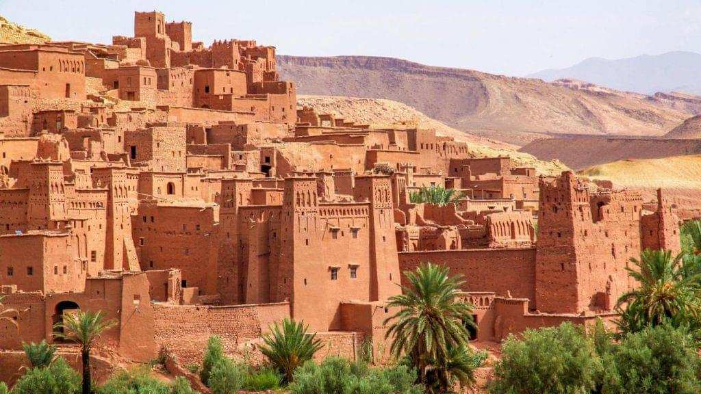 Historic Moroccan kasbah with traditional red clay walls, detailed patterns, and surrounding green palm trees on a desert landscape during 3 Days Tour from Fes to Merzouga.