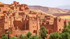 Historic Moroccan kasbah with traditional red clay walls, detailed patterns, and surrounding green palm trees on a desert landscape during 3 Days Tour from Fes to Merzouga.