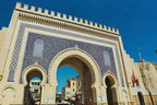 Traditional Moroccan city gate with beige stone and intricate blue tile mosaic archways under a clear sky for 3 Days Tour from Fes to Merzouga.