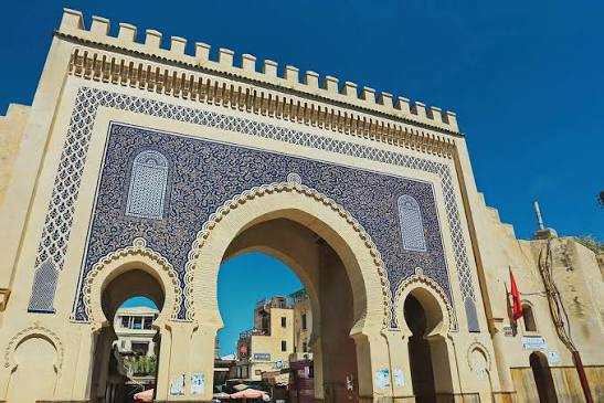 Traditional Moroccan city gate with beige stone and intricate blue tile mosaic archways under a clear sky for 3 Days Tour from Fes to Merzouga.