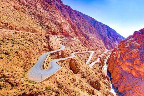 Winding mountain road through reddish rocky cliffs and deep gorge under clear blue sky during 3 Days Tour from Fes to Merzouga.