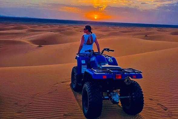 ATV quad bike in blue with a person in a white top riding at sunset across golden sand dunes, capturing a 3 Days Tour desert adventure.
