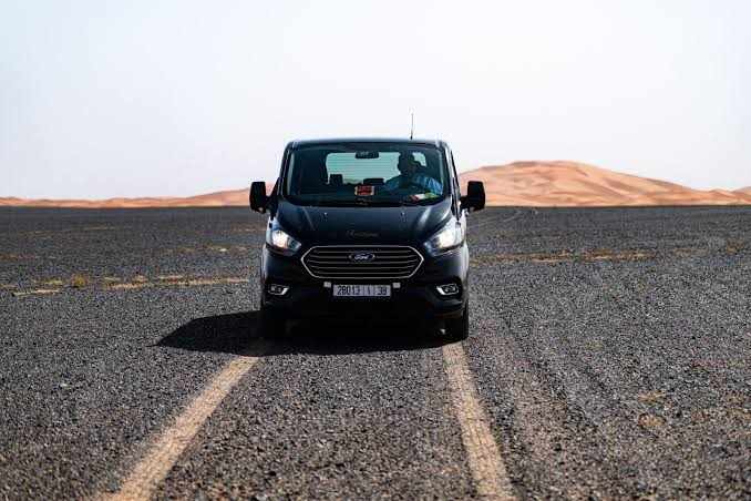 Black Ford passenger van driving on a gravel road toward sand dunes in the distance, illustrating the 3 Days Tour adventure.