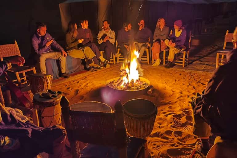 4-day desert tour group sitting around a campfire on sandy ground inside a desert tent at night