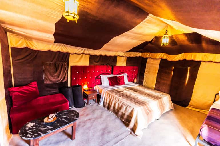 4-day desert tour luxury tent interior with brown and beige fabric walls, red tufted headboard, plush seating, and decorative lighting