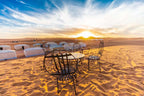 4-day desert tour metal table and chairs set on sandy dunes under a colorful sunset sky at a desert camp