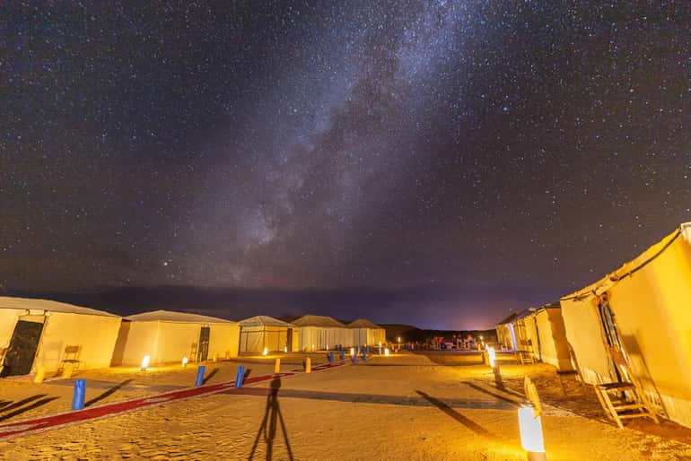 desert camp tents illuminated at night under a starry sky with the milky way visible, showcasing a serene desert experience for a 4-day desert tour
