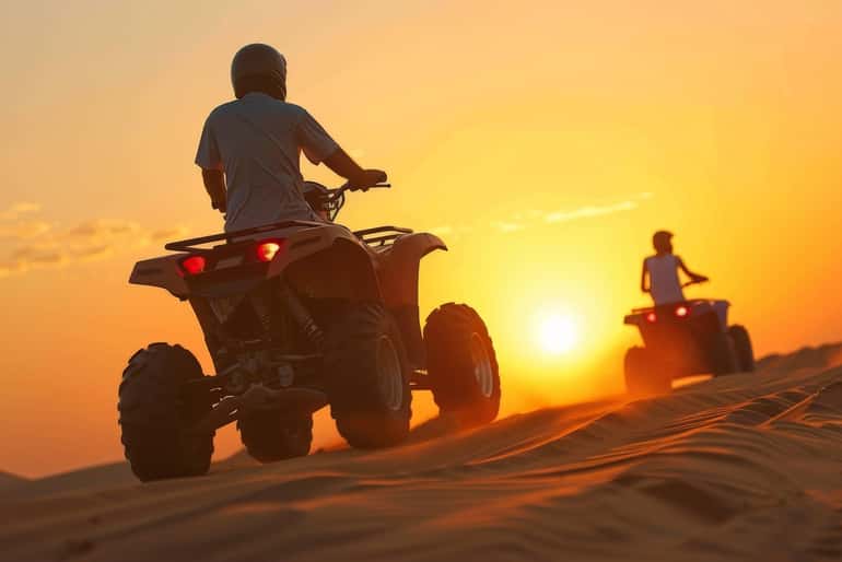 4-day desert tour with two people riding red quad bikes on sandy dunes at sunset with clear sky