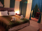 Bed with green and brown striped blanket and white pillows in a tented desert camp room softly lit with bedside lamps for 4-day desert tour