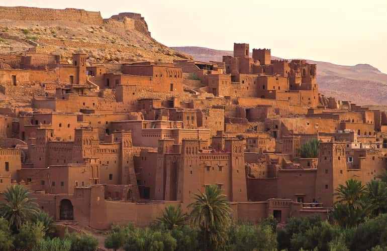 Traditional Moroccan kasbah made of brown earthen clay bricks with detailed patterns surrounded by palm trees and desert hills