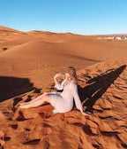 4-day desert tour featuring a woman in a white dress sitting on orange sand dunes under a clear blue sky in the Sahara desert