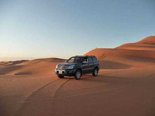 Black 4x4 SUV vehicle driving on orange sand dunes in the desert at sunset, illustrating 4x4 Rental in Merzouga