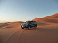 4x4 Rental in Merzouga black off-road vehicle parked on smooth orange desert sand dunes under clear blue sky