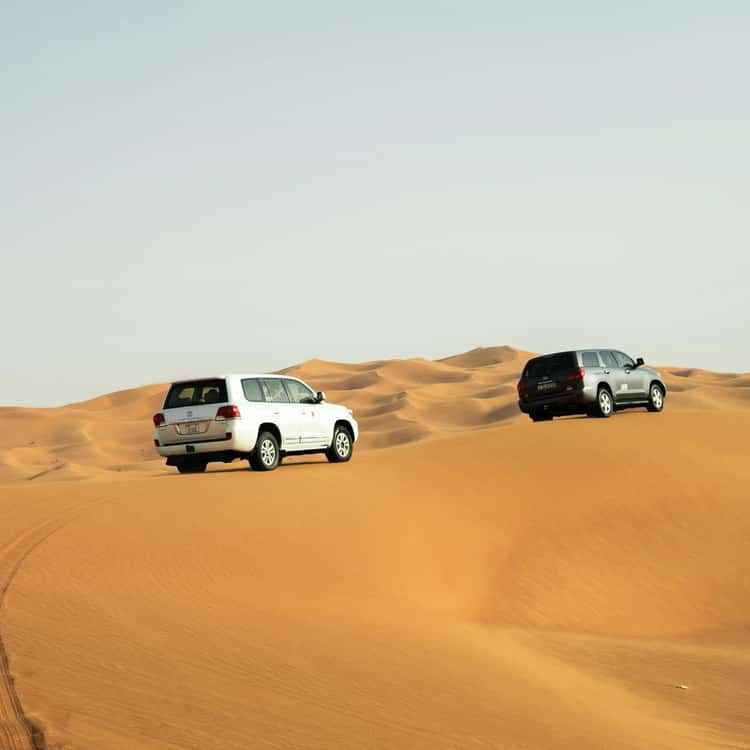 4x4 Rental in Merzouga showing white and black off-road vehicles driving on orange desert sand dunes under clear sky