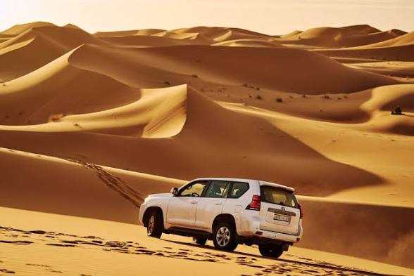 White 4x4 vehicle driving over golden sand dunes in the Moroccan Sahara desert during a 4x4 Transfer experience
