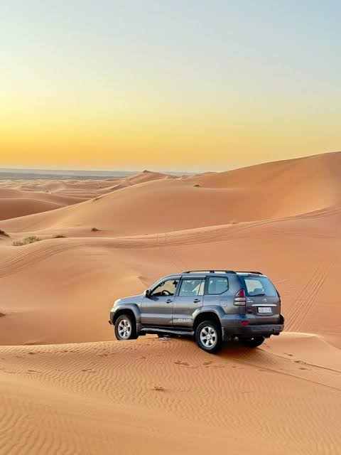 4x4 Transfer vehicle in silver parked on golden sand dunes under a clear sky in the Moroccan desert landscape