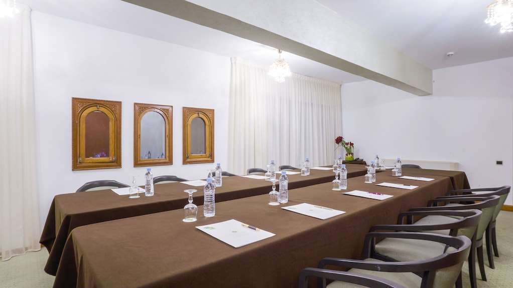 Conference room at Agadir Beach Club Hotel with brown tablecloths, black chairs, bottled water, notepads, and wooden framed mirrors