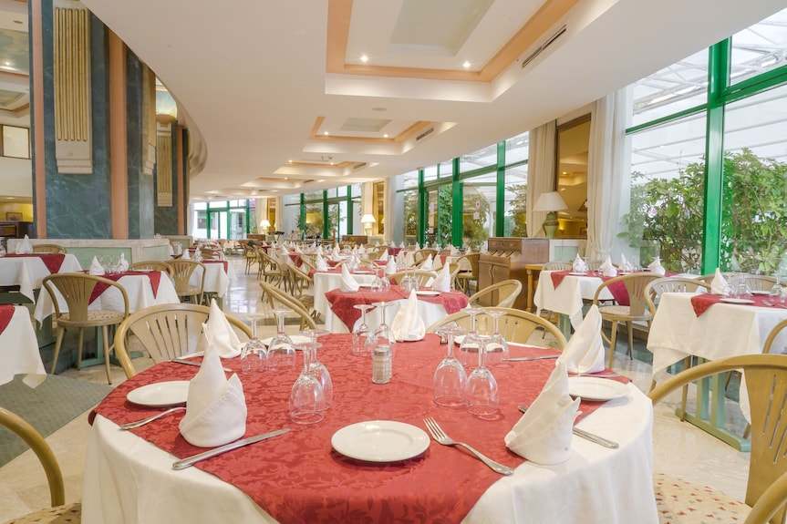 Spacious Agadir Beach Club Hotel dining area with white and red patterned tablecloths, beige chairs, and neatly arranged white napkins