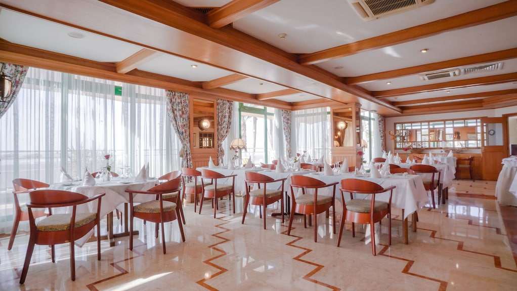 Dining area at Agadir Beach Club Hotel with wooden chairs, white tablecloths, floral curtains, and large windows