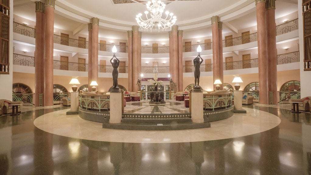 Spacious hotel lobby with tall brown columns, elegant chandeliers, classical statues, and ornate patterned flooring at Agadir Beach Club Hotel