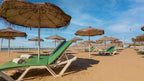 Agadir Beach Club Hotel sandy beach with green lounge chairs and thatched umbrellas under a blue sky