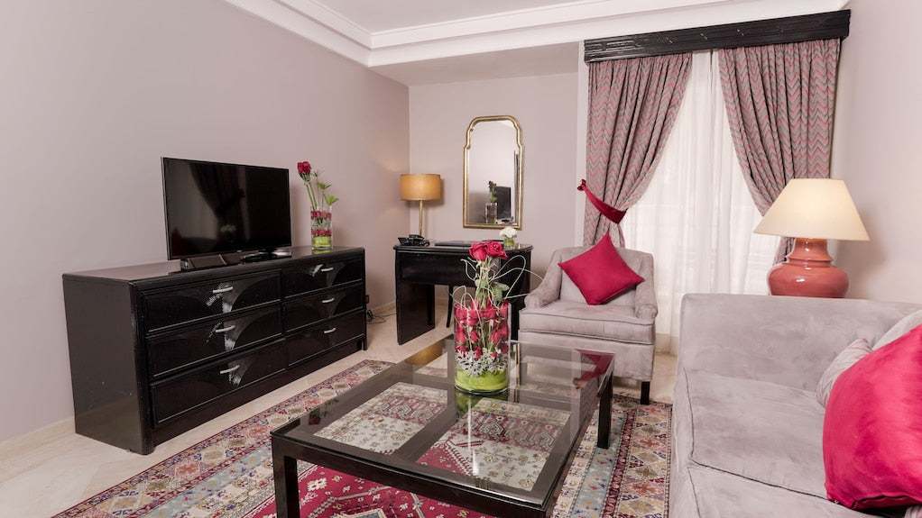 Agadir Beach Club Hotel living room with soft grey armchair and sofa, red cushions, glass coffee table on patterned rug
