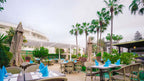 Outdoor dining area at Agadir Beach Club Hotel with beige wicker chairs, tables set with blue napkins, and palm trees