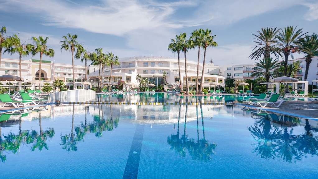 Agadir Beach Club Hotel large outdoor swimming pool with clear blue water, surrounded by green sun loungers and palm trees