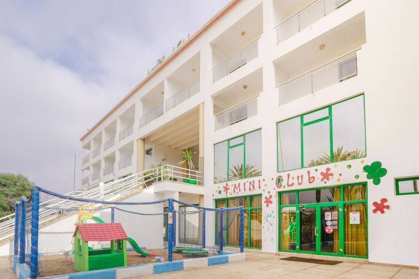 Agadir Beach Club Hotel white multi-story building with balconies and green-trimmed windows, featuring a colorful children's play area