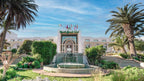 Agadir Beach Club Hotel with white facade, Moroccan-style arch entrance, surrounded by palm trees and green landscaping