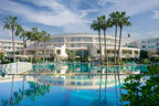 Agadir Beach Club Hotel large white resort building with palm trees and a blue swimming pool reflecting the sky and hotel