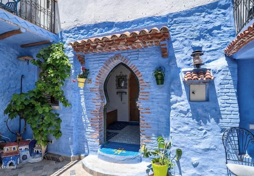 Alhambra Ryad & Spa blue-painted Moroccan riad entrance with brick arch, tiled steps, and green plants in Chefchaouen